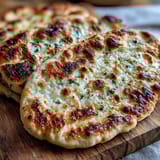 Stack of warm The Best Easy Garlic Naan Bread served beside a bowl of curry, perfect for scooping up rich sauce.