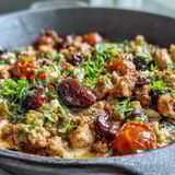 Sizzling ground chicken with Kalamata olives and cherry tomatoes in a skillet.