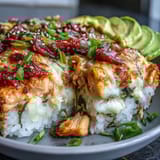 A close-up of creamy Spicy Salmon Sushi Bake topped with fresh avocado slices, ready to be scooped onto seaweed snacks.