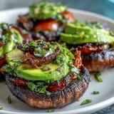 Hearty grilled portobello burgers topped with creamy avocado, perfect for cookouts.