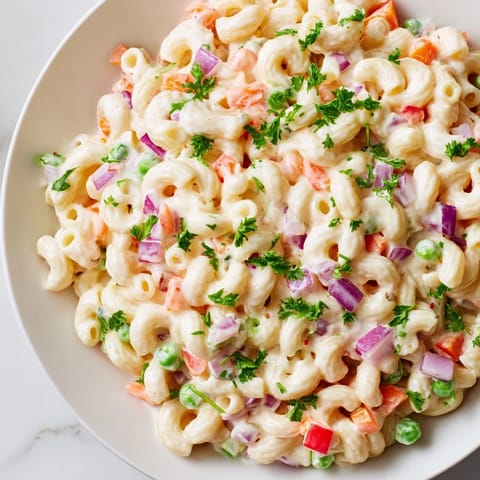 A vibrant bowl of classic macaroni salad, with visible celery and red bell peppers.