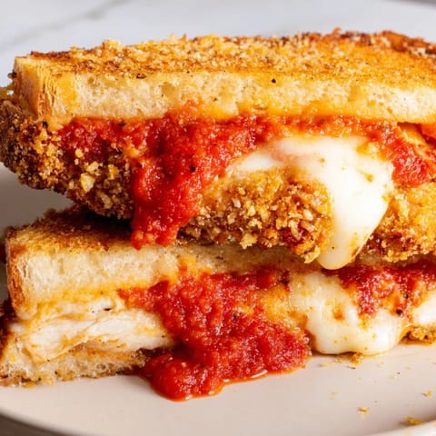 A close-up of a Chicken Parm Grilled Cheese, showcasing the gooey mozzarella pull and rich red marinara sauce dripping from the edges.  