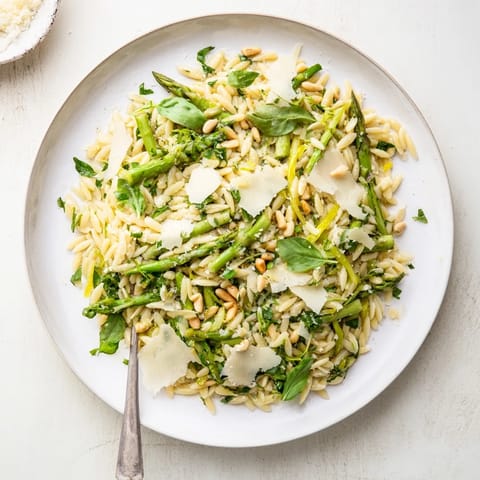 Shaved asparagus ribbons and tender orzo pasta are tossed in a bright lemon-olive oil dressing for this vibrant Asparagus Lemon Orzo Salad, garnished with grated Parmesan and toasted pine nuts.