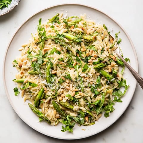 A close-up of the vegetarian Asparagus Lemon Orzo Salad highlights fresh herbs and glistening lemon dressing clinging to each grain and crisp green ribbon.