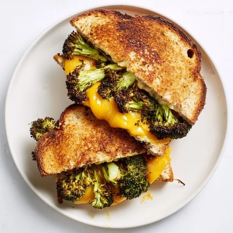 Buttery sourdough slices hold gooey cheddar and caramelized broccoli pieces, served warm beside a steaming bowl of tomato soup for dipping.  