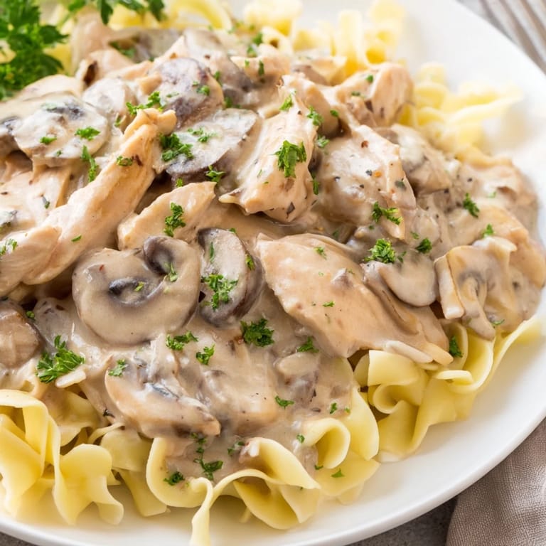 A close-up of Chicken and Mushroom Stroganoff reveals tender meat and earthy fungi, with a garnish of fresh parsley and a fork ready to serve.