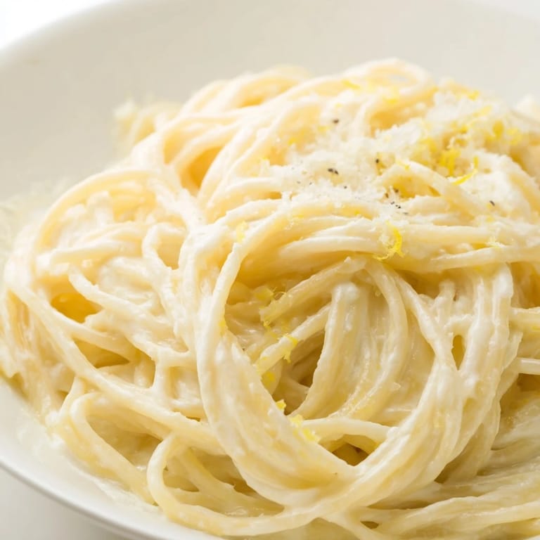 Tossing hot spaghetti with the zesty lemon sauce, garnished with fresh basil and extra Parmesan.