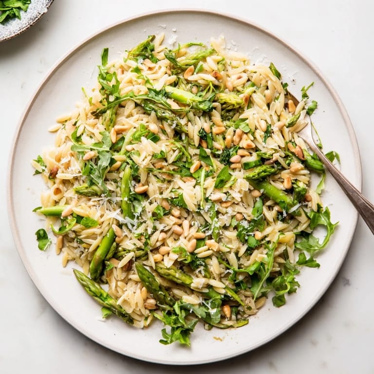 A close-up of the vegetarian Asparagus Lemon Orzo Salad highlights fresh herbs and glistening lemon dressing clinging to each grain and crisp green ribbon.