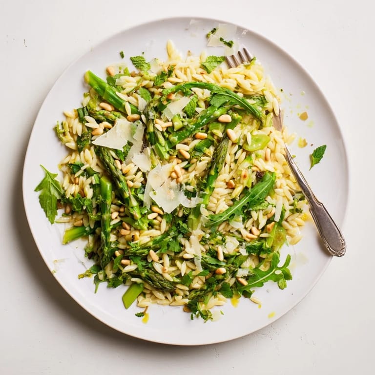 Perfect for spring and summer gatherings, the Asparagus Lemon Orzo Salad is served in a white bowl with extra Parmesan and a lemon wedge.