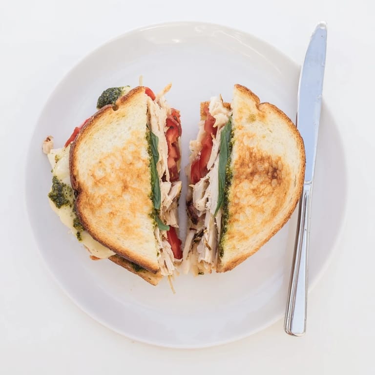 A close-up of a perfectly grilled Mozzarella Pesto Chicken Grilled Cheese, showing gooey mozzarella and savory shredded chicken inside toasted bread.