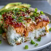 Golden-baked Spicy Salmon Sushi Bake fresh from the oven, with melted cheese and sesame seeds on a bed of seasoned rice.