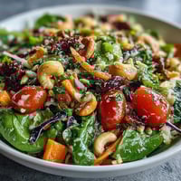 Bright and colorful Rainbow Salad Bowl in a white bowl, featuring quinoa, cherry tomatoes, purple cabbage, and chickpeas, ready for a nutritious vegan lunch.